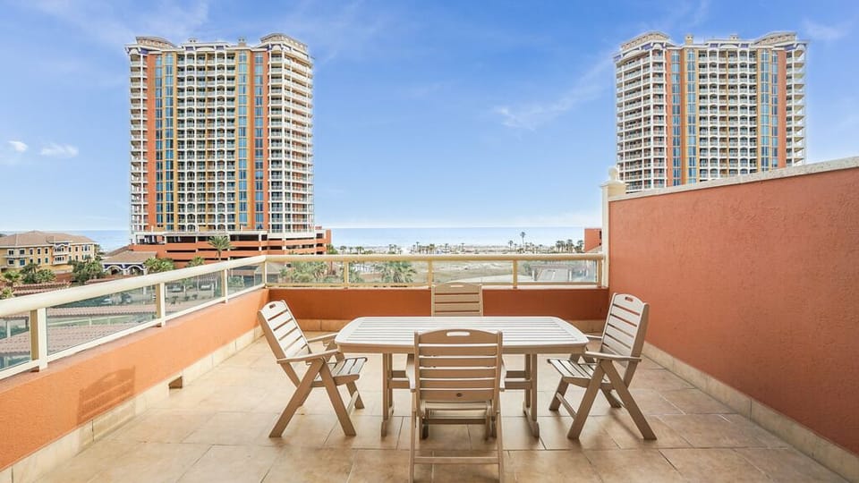 Your private terrace offers outdoor dining space with seating for four, framed by sunny skies and glimpses of palm-lined surroundings—perfect for morning coffee or evening meals in the warm air.