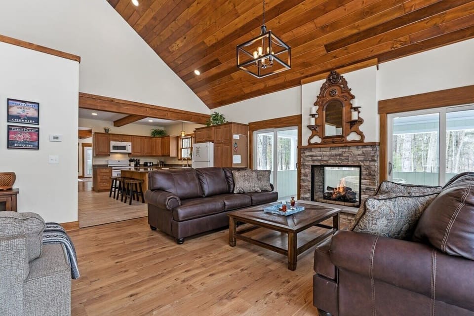 Living room with double-sided glass fireplace. Screened porch is accessed to the right, kitchen is ahead, TV is on the left with stairs to the basement rec room.