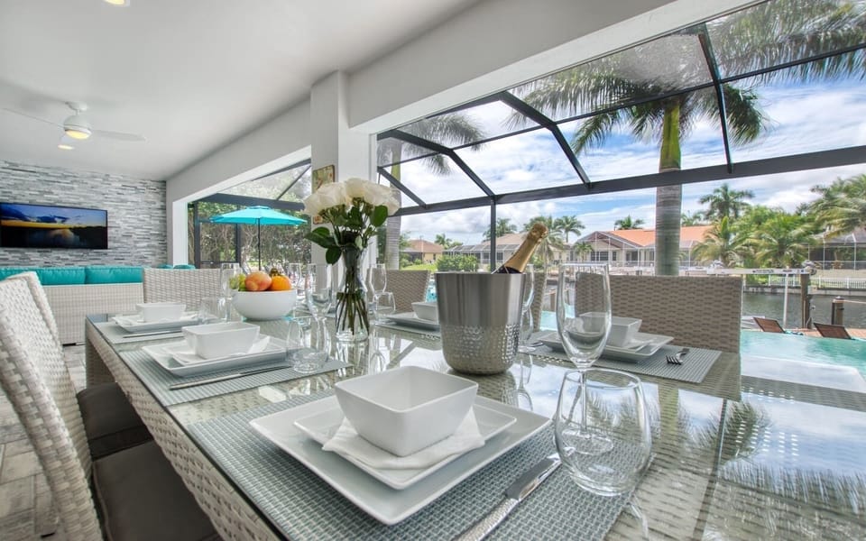 Outdoor dining table set with plates, glassware, and a centerpiece arrangement under the screened enclosure