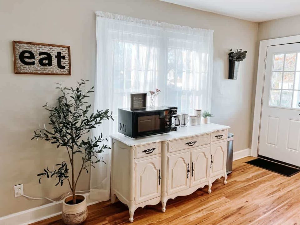 - Kitchen corner with microwave coffee maker and storage   - White vintage cabinet with natural light from windows   - Convenient setup for quick snacks and fresh coffee  