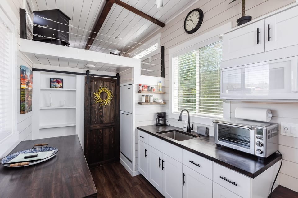 Bright, modern kitchen with a full-size sink, ample counter space, microwave, and coffee maker. Clean design and natural light make meal prep easy and comfortable during your tiny home stay.