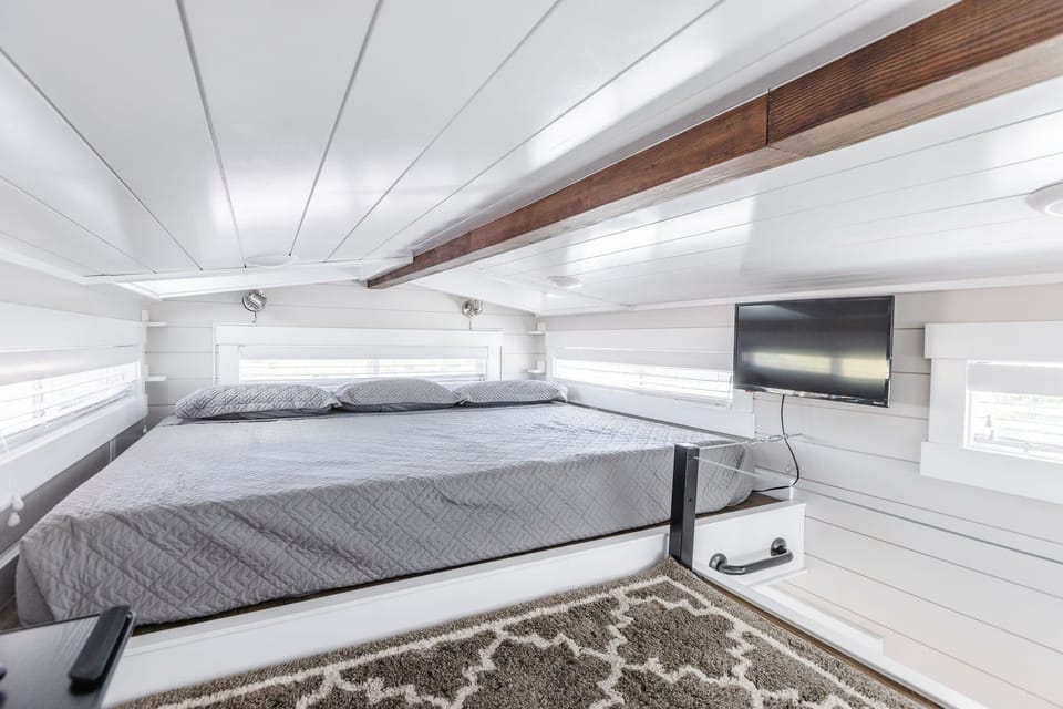 King-size bed in loft-style Bedroom 2, accessed by stairs from the living area. Includes soft linens, built-in storage, and a wall-mounted TV for comfort in this elevated sleeping space.