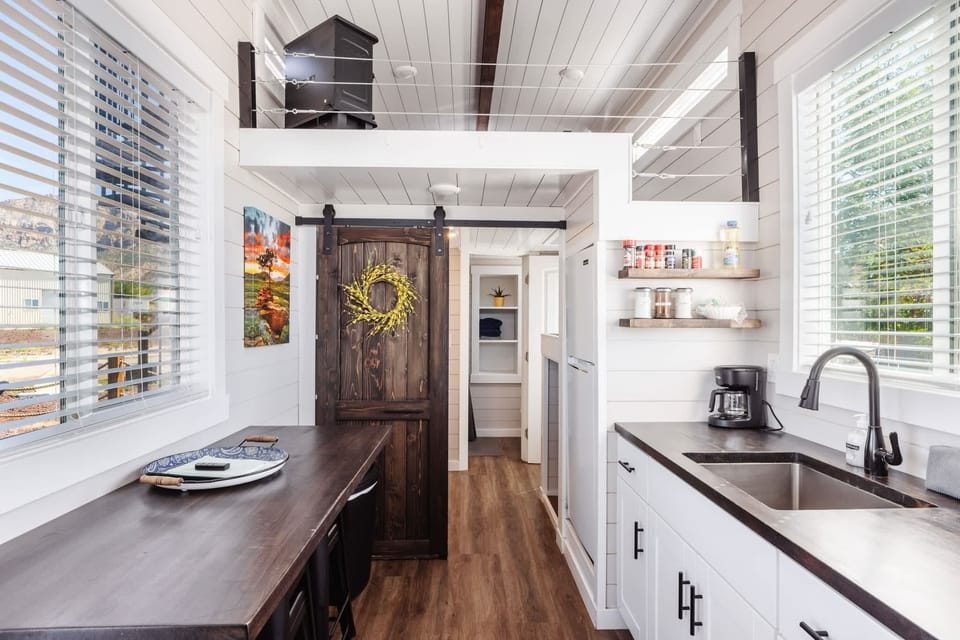 Compact dining area integrated with the kitchen, featuring a functional table, open shelving, and abundant natural light. Designed for easy meals and relaxed dining in a thoughtfully laid-out space.