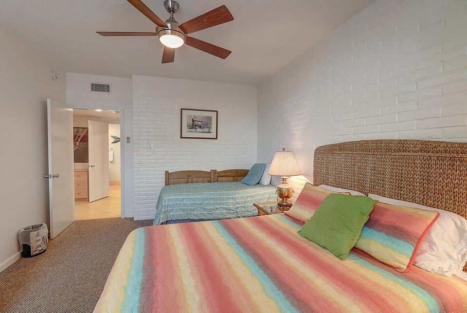 Drift into comfort in your airy bedroom, where colorful bedding meets coastal charm and gentle ceiling fan breezes create your perfect retreat.