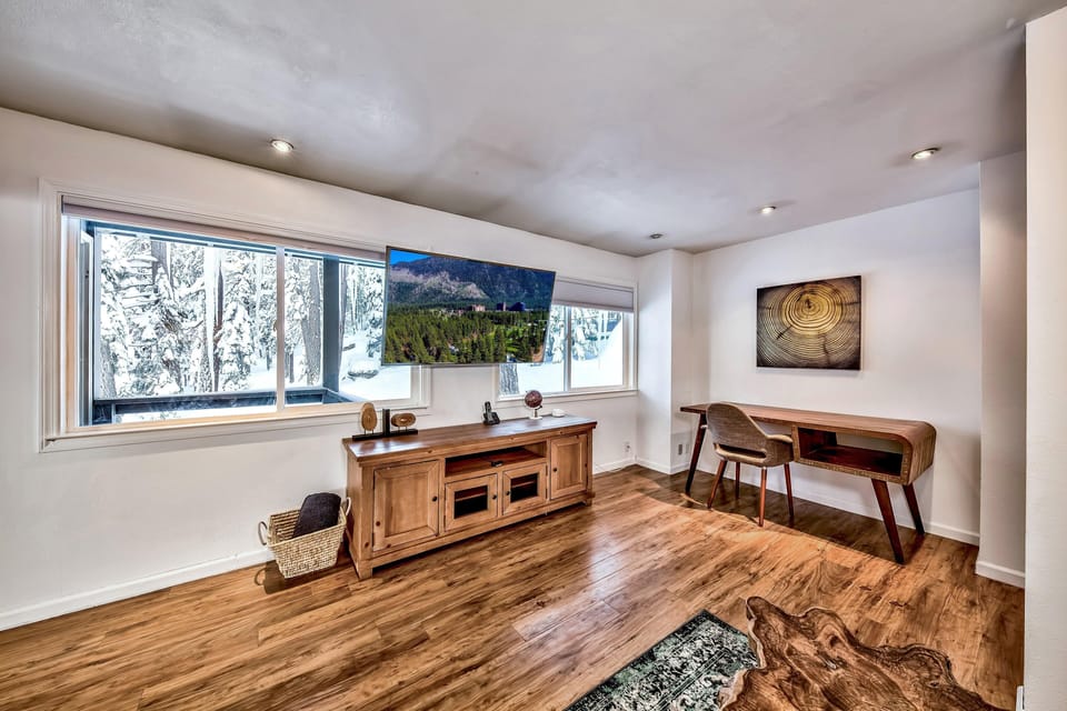 Media room with wall-mounted TV above wooden console, hardwood floors, and a mid-century modern desk with chair.