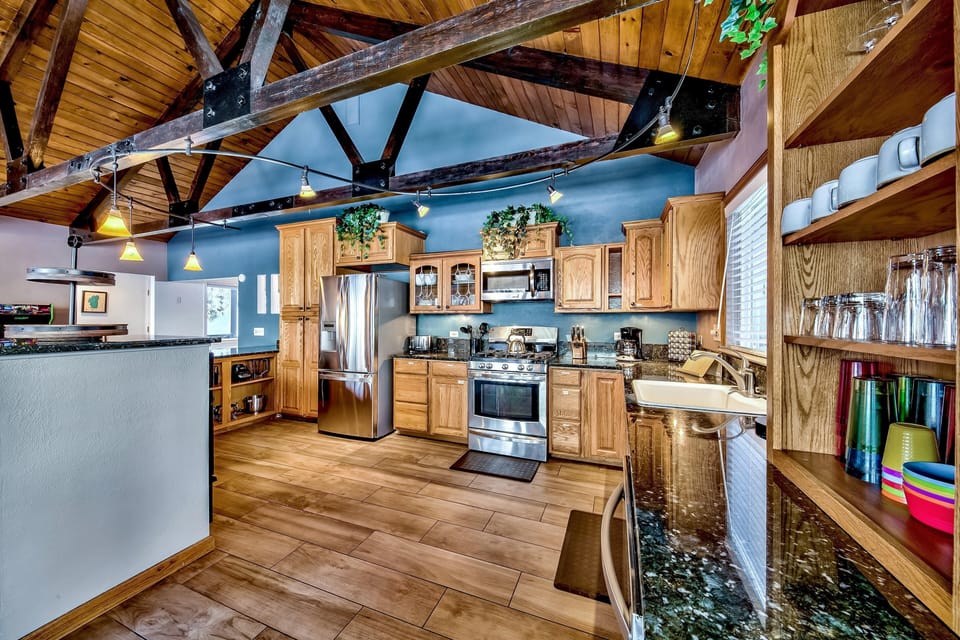 Kitchen with oak cabinetry, stainless steel appliances, black granite countertops, and exposed dark wood beams.