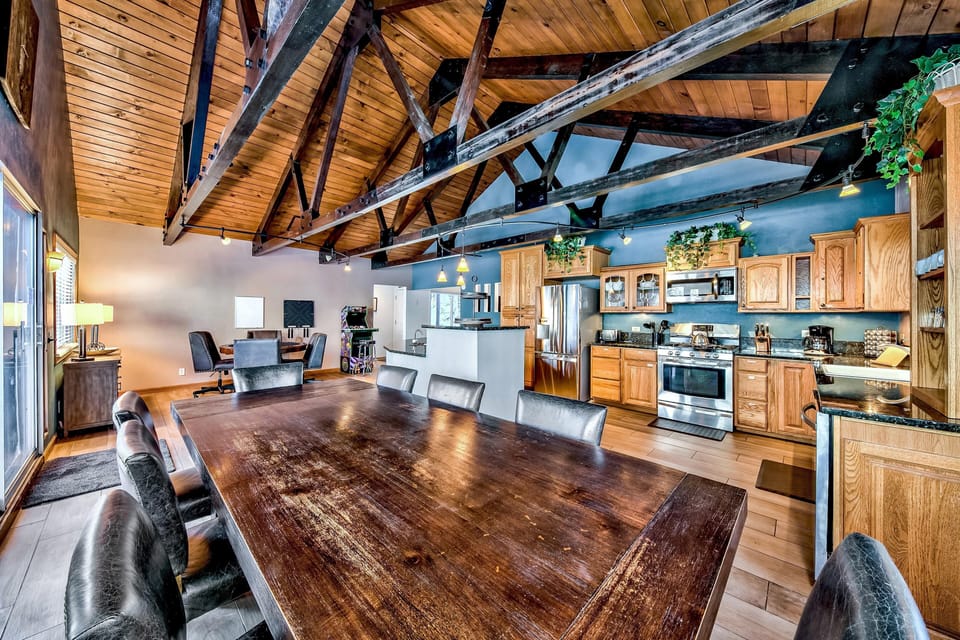 Vaulted wood ceiling with black metal beams spans the kitchen and dining area featuring oak cabinets and granite counters.