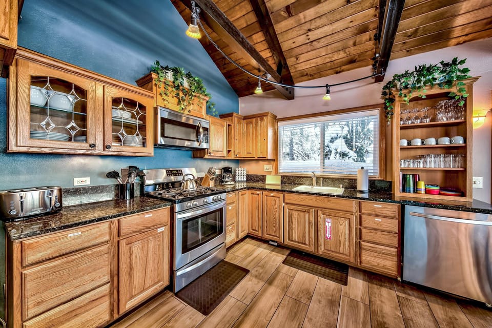 Wood-paneled vaulted ceiling with exposed beams and track lighting highlights the kitchen’s glass-front cabinets.