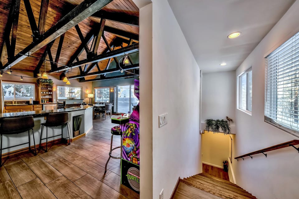Wood staircase with angular handrail leads down from a brightly lit landing with windows and potted greenery.