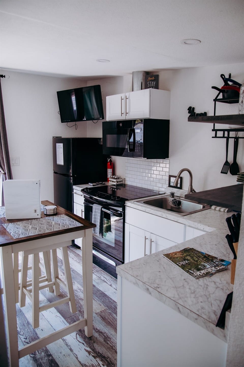 This angle of the kitchenette has sleek white cabinetry paired with a marble-inspired countertop and classic subway tile backsplash. The space is fully equipped with a gas range, microwave, and a deep stainless steel sink for a great experience.