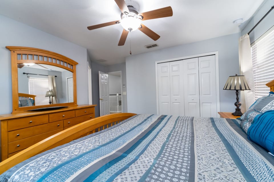 Upstairs bedroom with wood bed frame, ceiling fan, dresser with mirror, and closet.