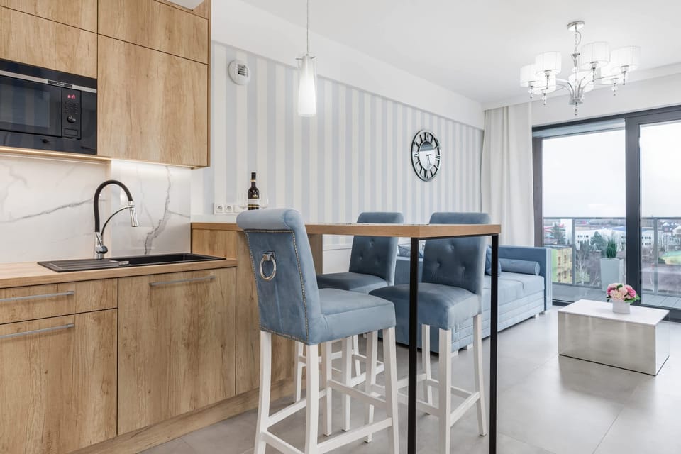 A compact kitchen area with light wooden cabinets, a marble backsplash, and blue upholstered bar stools at a breakfast bar.