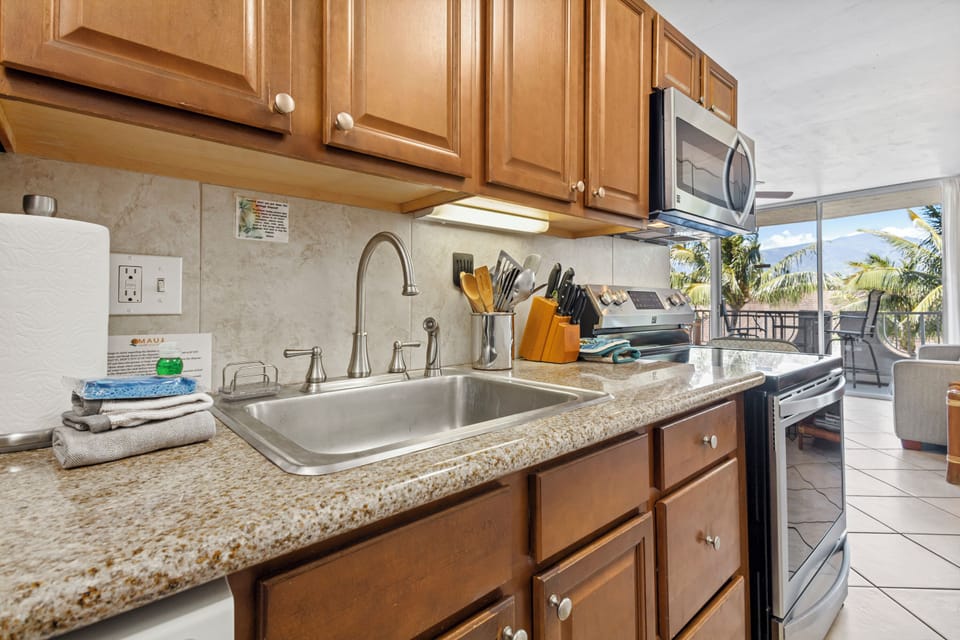 Your fully equipped kitchen offers everything you need to prepare fresh meals, with granite counters, stainless steel sink, modern appliances, and a stunning balcony view beyond.