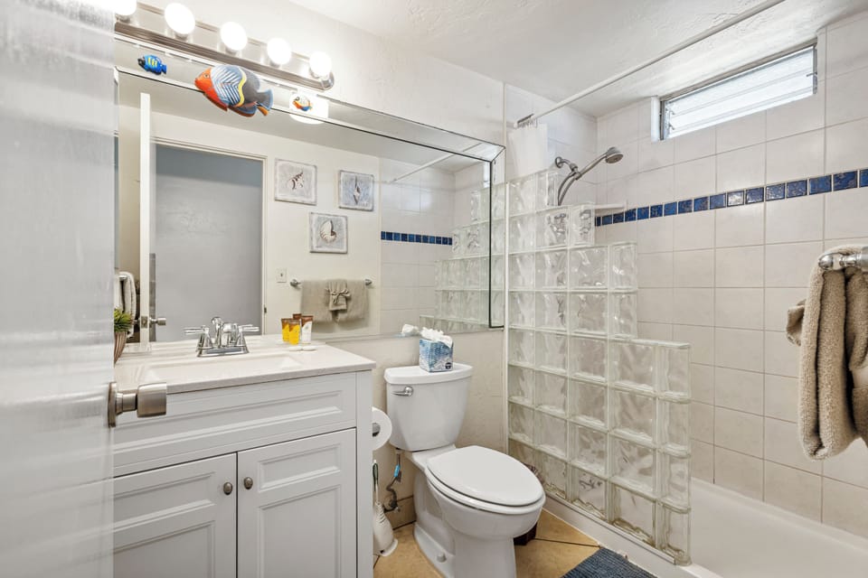 Your bright, coastal-themed bathroom features a sparkling glass block shower, blue tile accents, and cheerful fish decor—perfect for freshening up after beach adventures.
