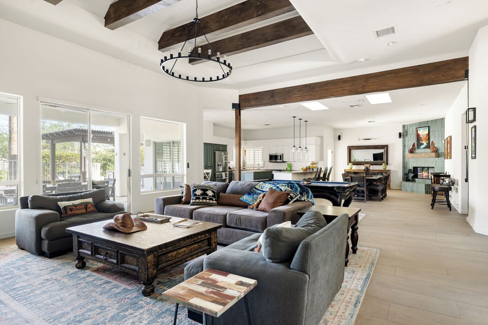 Open-concept great room with soaring ceilings, exposed wood beams, and abundant natural light. Seamlessly connecting the living, dining, and kitchen areas, it's the perfect space for gathering, entertaining, and relaxing together.