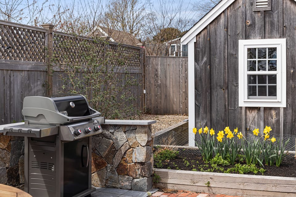Gas grill on brick patio and garden.