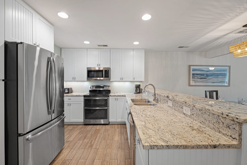 Crisp white cabinetry, stainless steel appliances, and a clean tile backsplash give the space a fresh, coastal feel.