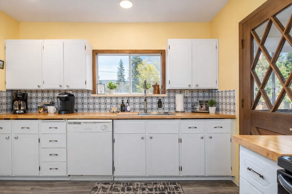 Your bright kitchen features white cabinetry, wood countertops, and charming patterned backsplash with natural light streaming through garden views.