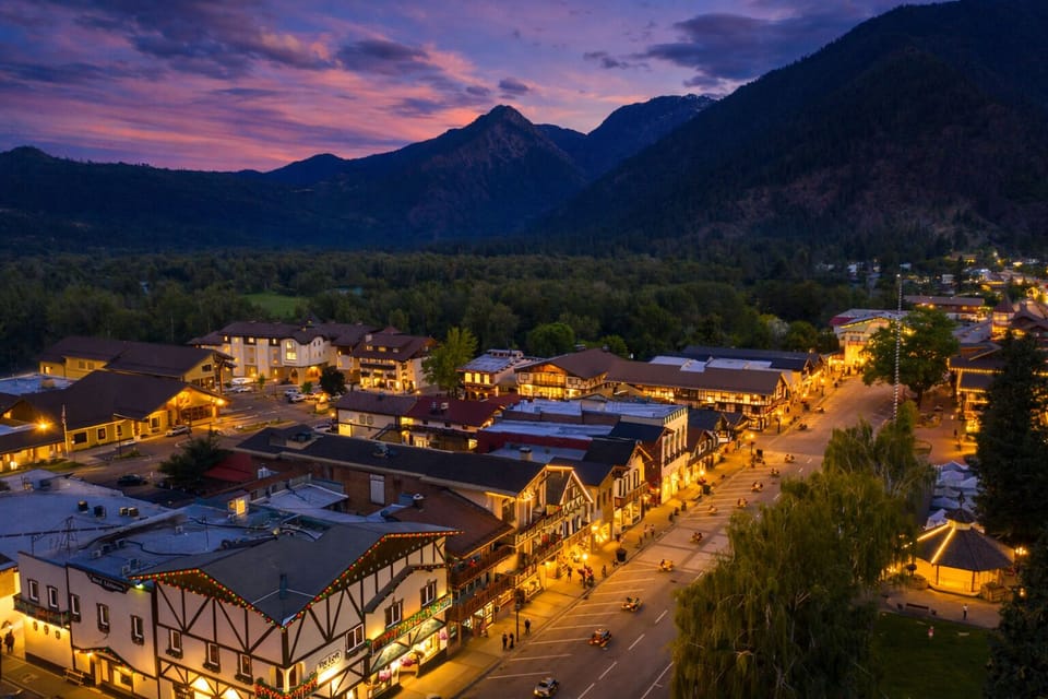Charming mountain town of Leavenworth, Washington nestled in a dramatic valley, with illuminated buildings creating a warm glow against the stunning purple sunset sky.