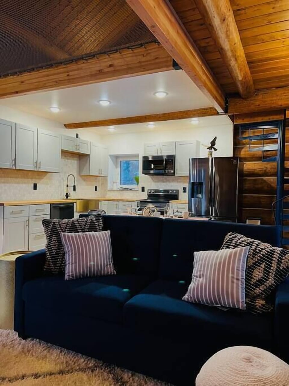 A cozy living room with a navy sofa, patterned pillows, and a modern kitchen view.