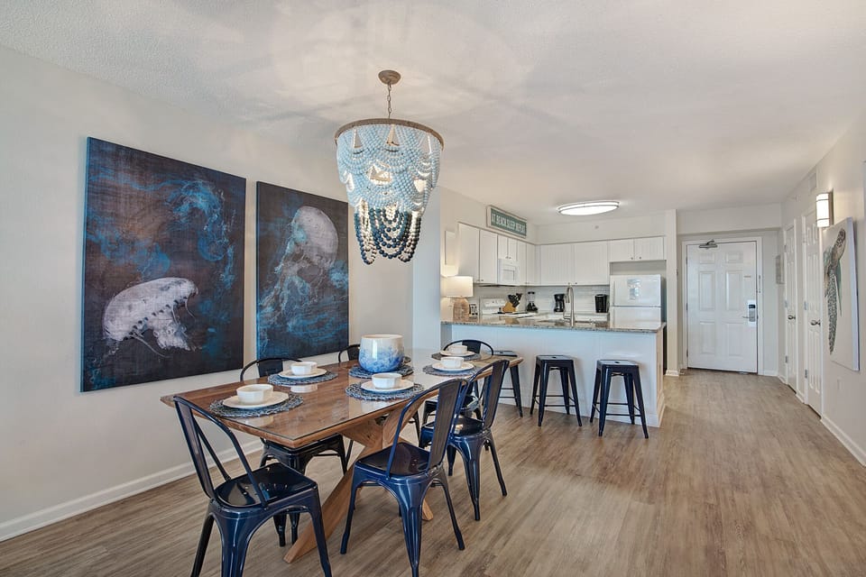 Your coastal-inspired dining space flows seamlessly into the modern kitchen, perfect for memorable meals with ocean-themed art setting the mood.