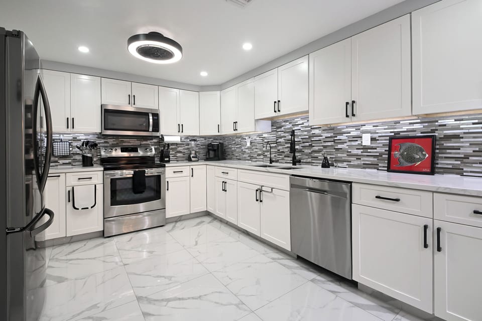 Cook your favorite meals in this modern kitchen featuring gleaming white cabinets, stainless steel appliances, and striking backsplash tile.