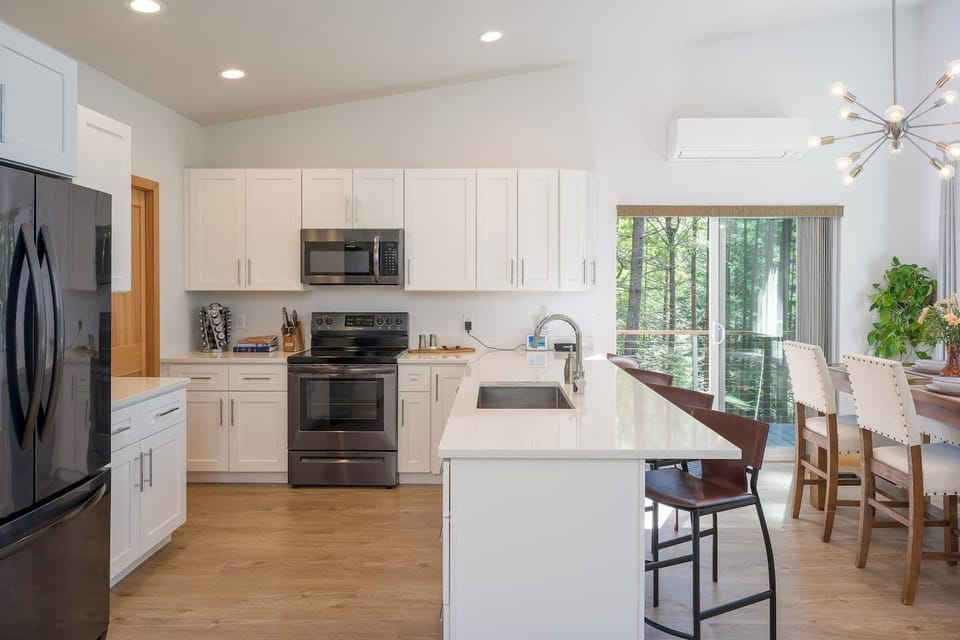 A fully equipped chef's kitchen — quartz island, stainless appliances, and a forest view while you cook.