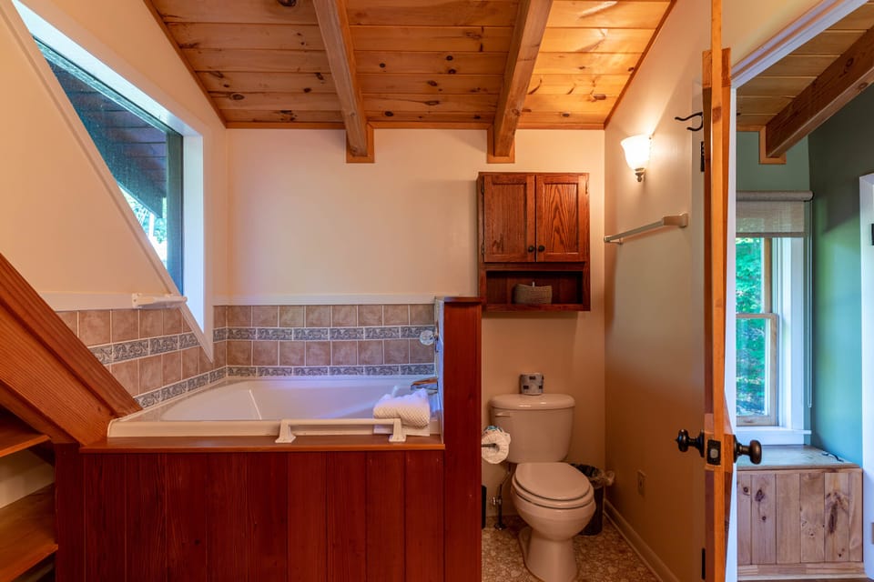 Rustic charm meets relaxation in this cabin bathroom, where a deep soaking tub sits beneath a bright window framed by warm wood.