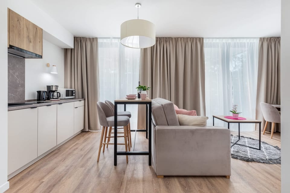 A living area with floor-to-ceiling windows, light furniture, and a cozy seating arrangement.
