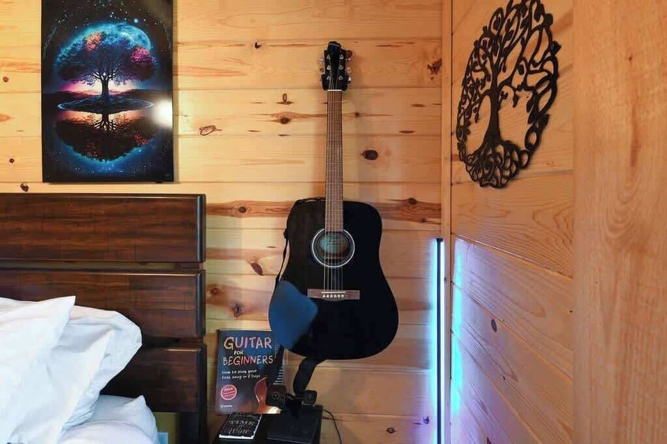 Cozy wooden room corner featuring a black acoustic guitar and artistic wall decor.
