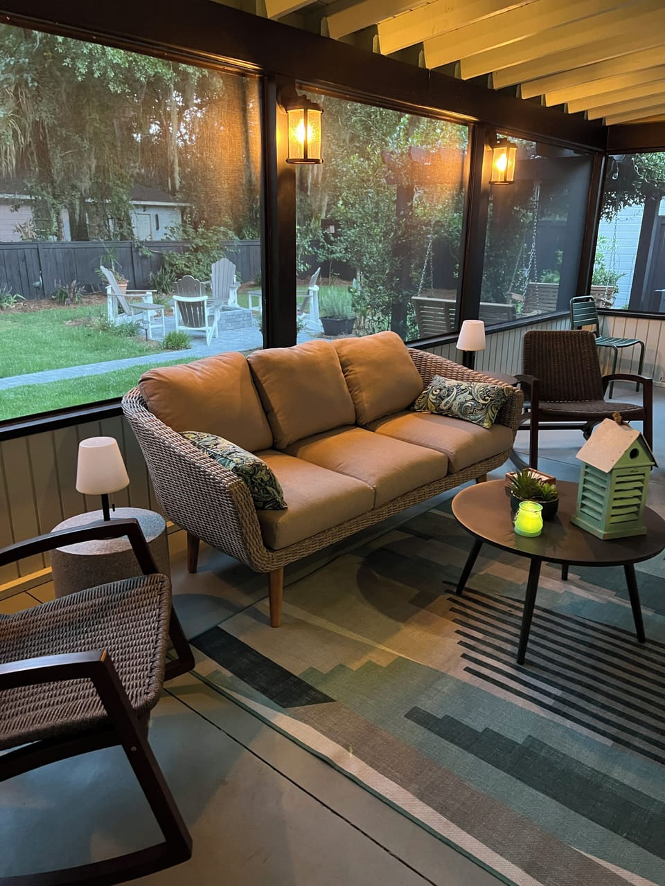Screened porch with couch, 2 rockers, TV, dining table, ambiant night lighting