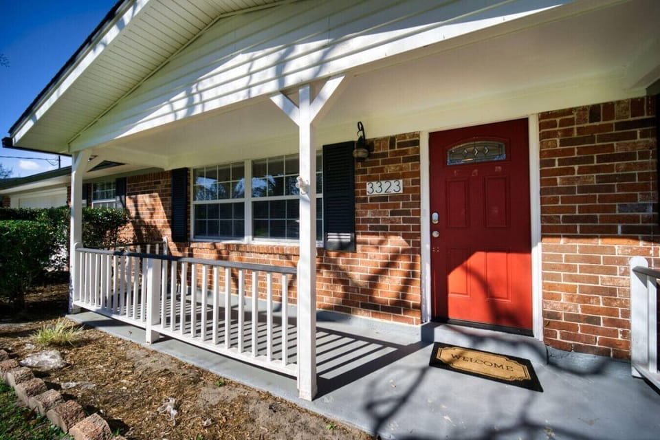 Welcoming front porch with charming brick accents, a bold red door, and cozy seating potential.