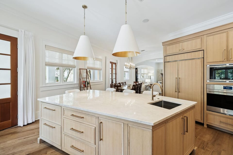 Large kitchen island with marble countertop, brass faucet, and two white pendant lights with gold interiors.