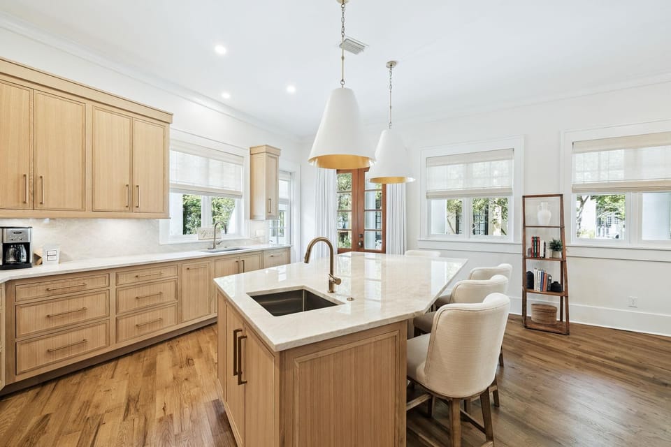 Light-filled kitchen island with marble countertop, built-in sink, and four upholstered stools beneath pendant lights.