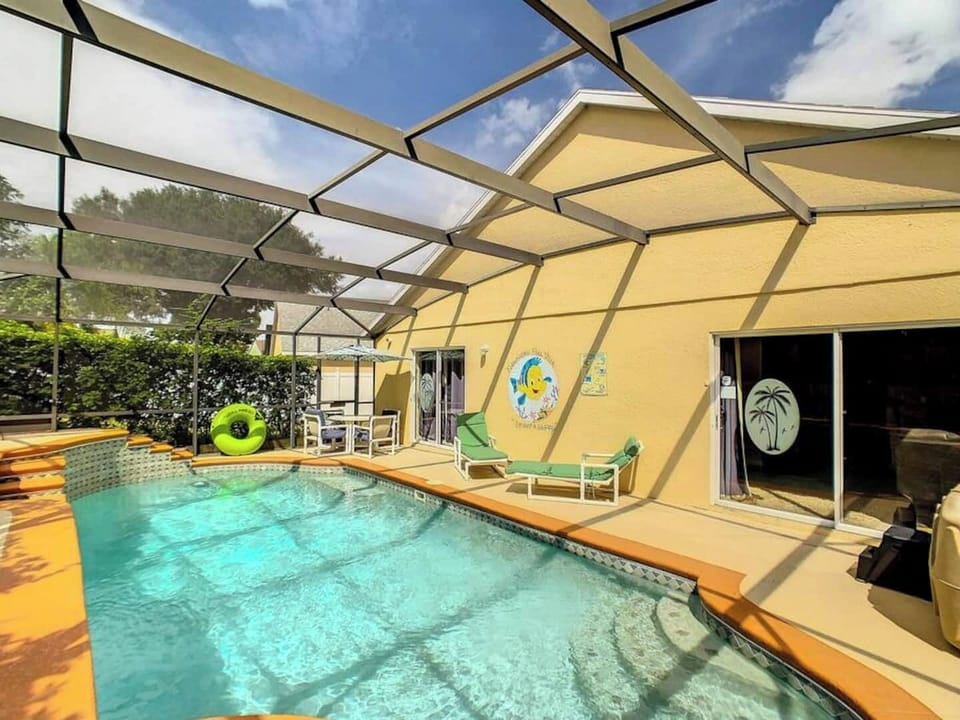 Pool area with a screened enclosure. There is a pool, lounge chairs, and a small dining set.