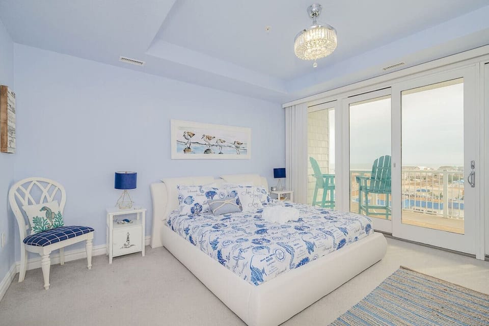 Wake up to breathtaking beach views in this cozy coastal king bedroom 🌅 Sliding doors open to your private balcony with Adirondack chairs perfect for morning coffee ☕️🐚
