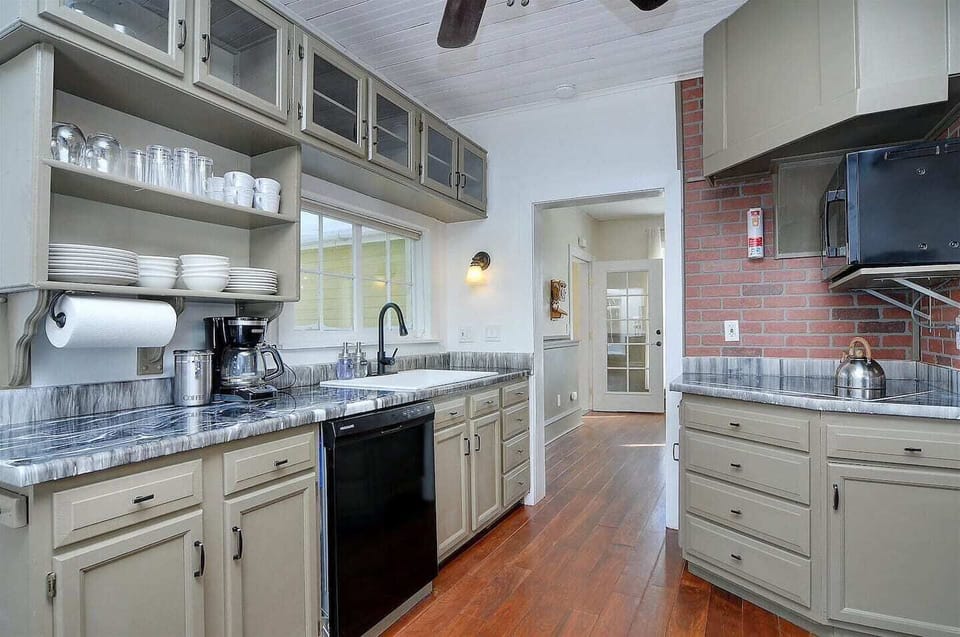- Well equipped kitchen with open shelving, dishes, and a full suite of appliances
- Earth toned cabinets, exposed brick backsplash, and wood floors add character
- Bright and functional layout ideal for meal prep and morning coffee routines