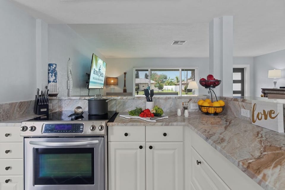 Bright and inviting kitchen featuring crisp white cabinetry, sleek stainless steel appliances, and a spacious wrap-around breakfast bar perfect for casual dining and entertaining.