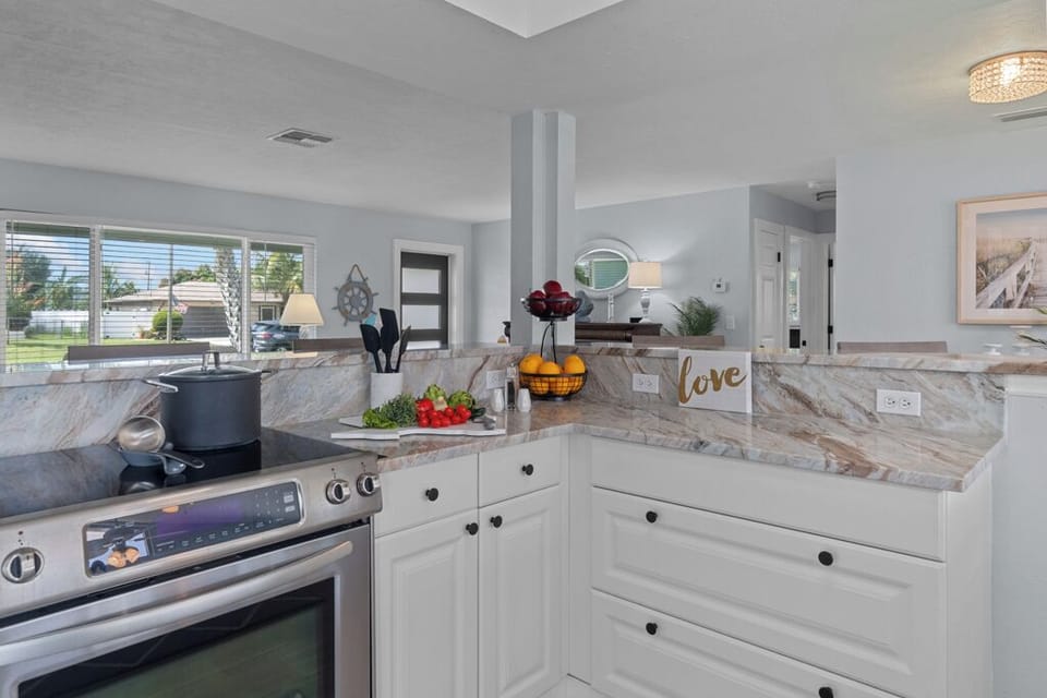 Bright and inviting kitchen featuring crisp white cabinetry, sleek stainless steel appliances, and a spacious wrap-around breakfast bar perfect for casual dining and entertaining.