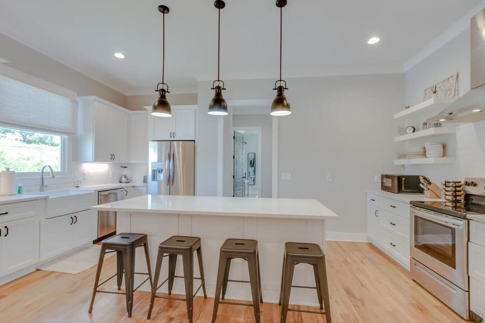 The modern farmhouse kitchen features a large island, bar stools, and fresh white cabinetry.