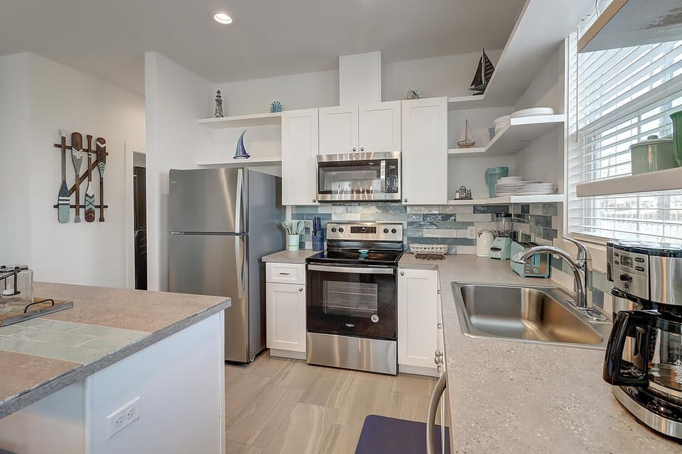 Your fully equipped kitchen features granite countertops, stainless steel appliances, and coastal decor perfect for preparing vacation meals together.