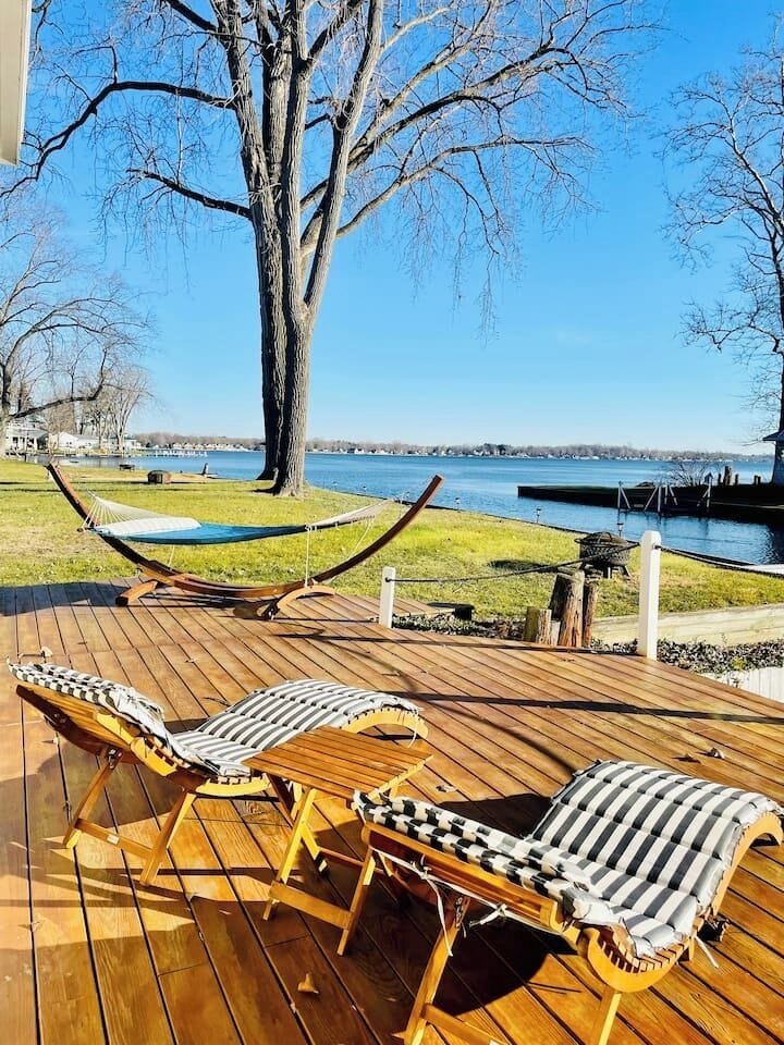 Large lakeside deck with lounge chairs overlooking the water.
