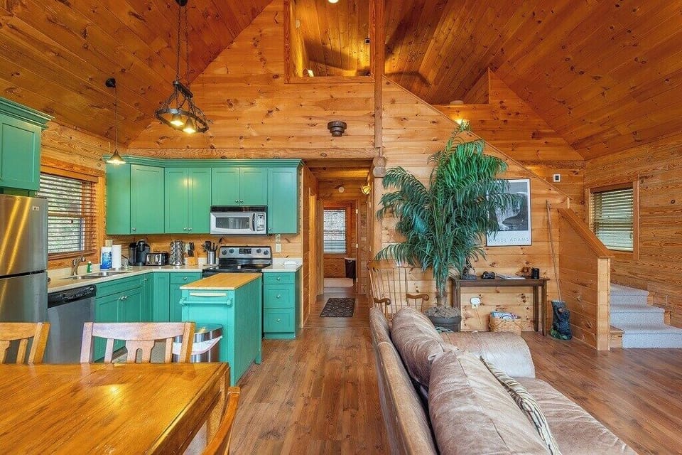 Open floor plan with big windows, a beautiful kitchen, dining room table, and cozy couch.