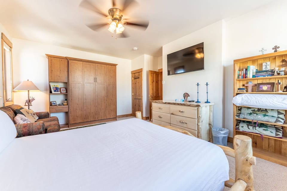 Drift off in your cozy bedroom with rustic wood furnishings, wall-mounted TV, and thoughtful touches that create the perfect mountain retreat atmosphere.