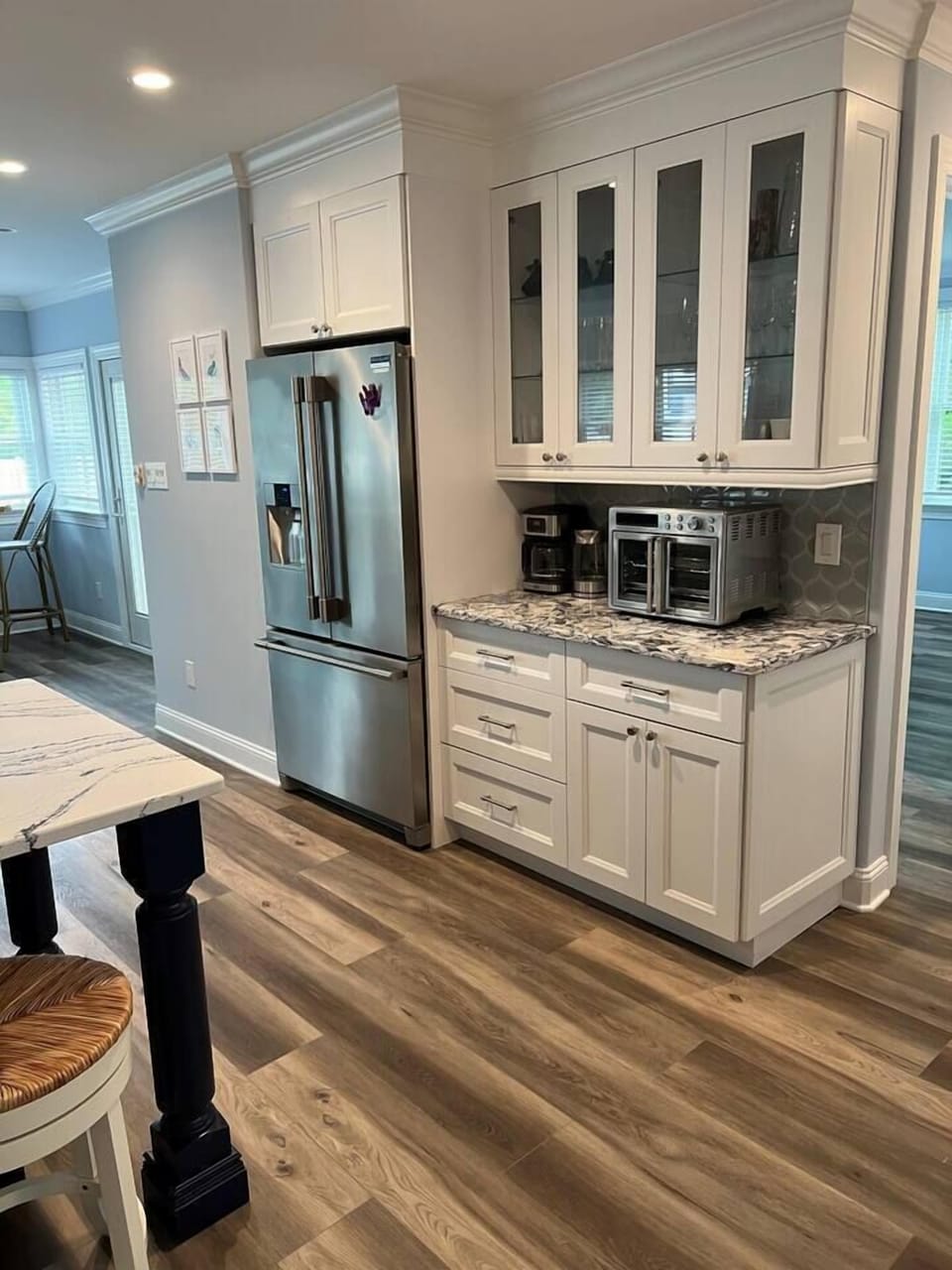 View of kitchen from near dining room table.  Drip coffee maker, water kettle and high end toaster oven can be seen.  Plenty of glasses and stemware in cabinets above.