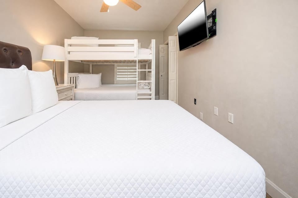 Cozy guest bedroom featuring a queen bed, a bunk bed with two queens, and a flat-screen TV for entertainment