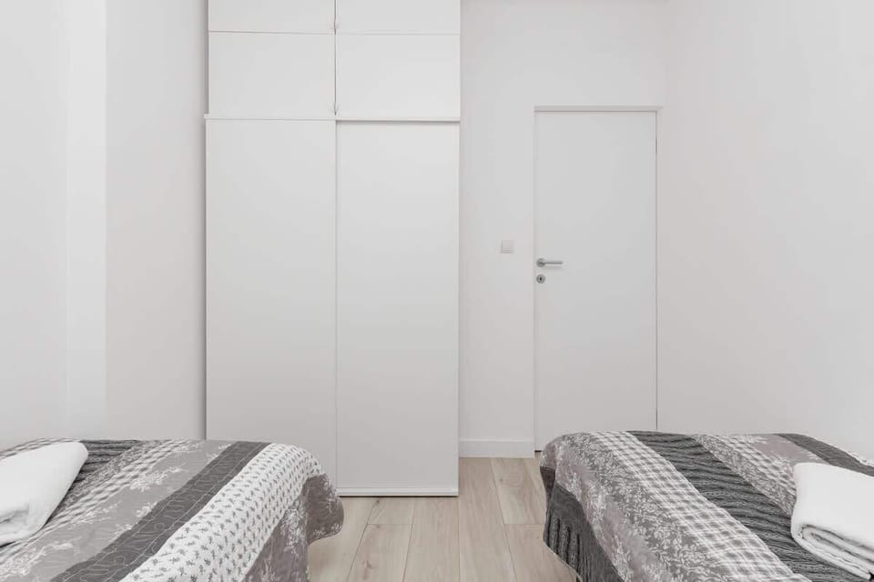 A spacious and well-lit bedroom featuring a two single beds, storage solutions, and  closet.