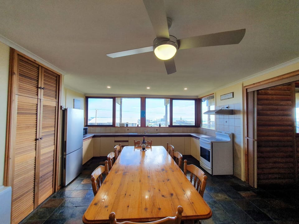 Includes a large front deck with sea views, a pergola-covered dining space, fire pit, paved and grassed backyard zones, outdoor shower, and a dedicated surfboard rack.