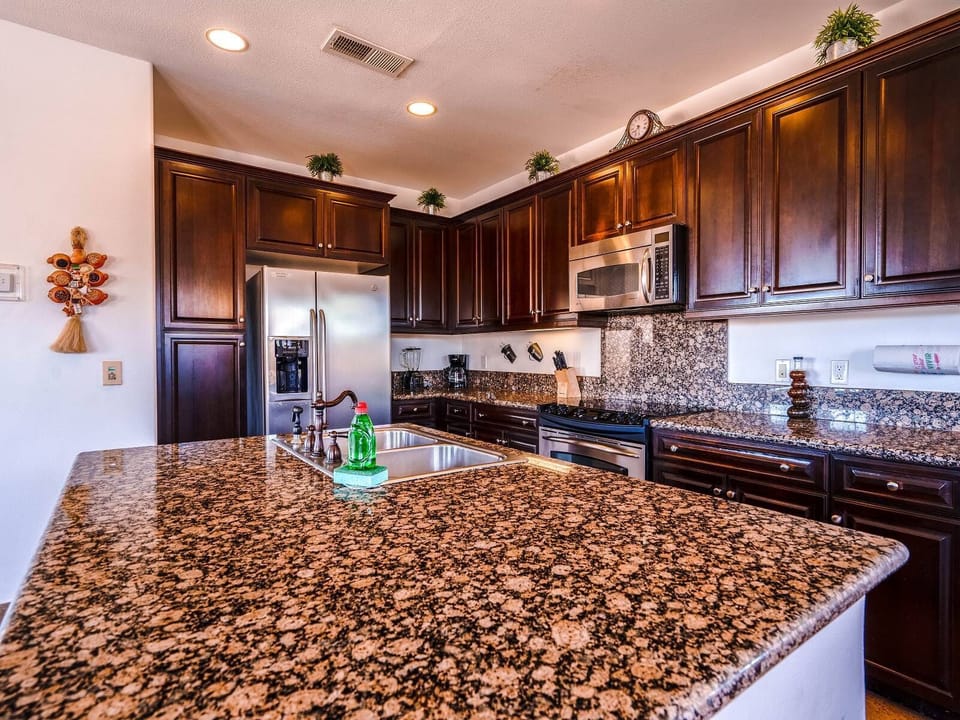 The chef's kitchen includes a breakfast bar, full-size refrigerator, gas stove, double sinks, microwave, coffee maker, and dishwasher. It's fully stocked with cookware, dishes, and tableware.
