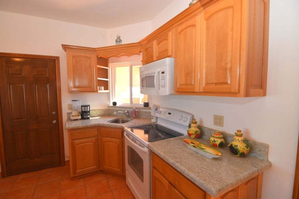 Condo B features an upstairs kitchen with snack bar seating for nine, a separate dining area, a spacious living room with large windows, and two bedrooms with private bathrooms — one with two queen beds and one with a single queen bed